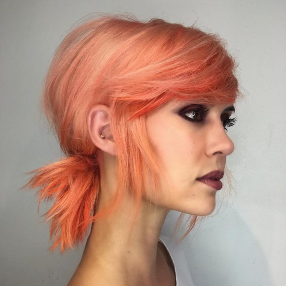 Low Messy Textured Ponytail with Side Swept Bangs and Pink Coral Hair Color