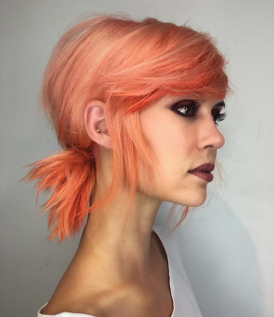 Low Messy Textured Ponytail with Side Swept Bangs and Pink Coral Hair Color Medium Length Updo Hairstyle